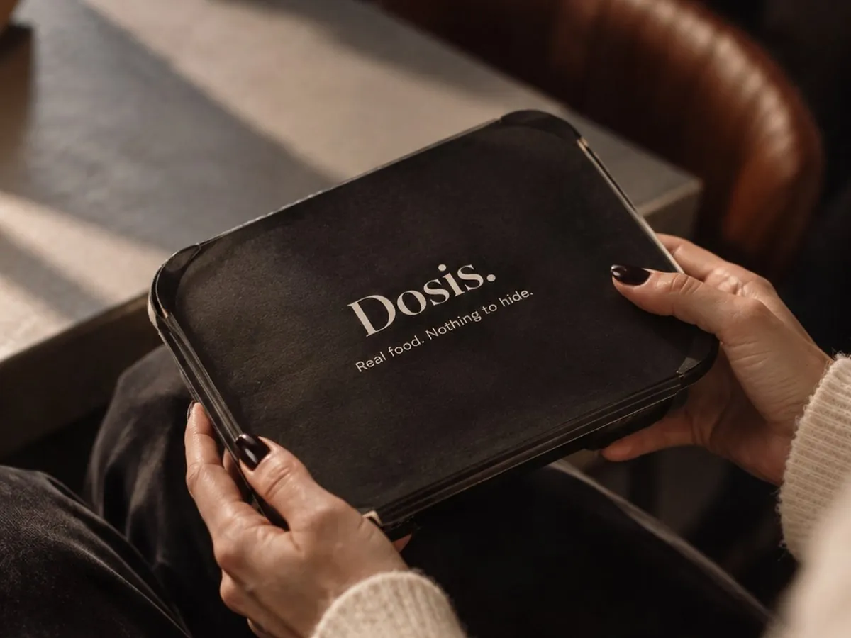 Hands holding a closed black Dosis. takeaway tray with the line "Real food. Nothing to hide."