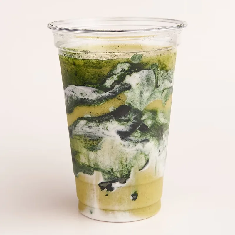 A green smoothie swirled with white in a clear cup.